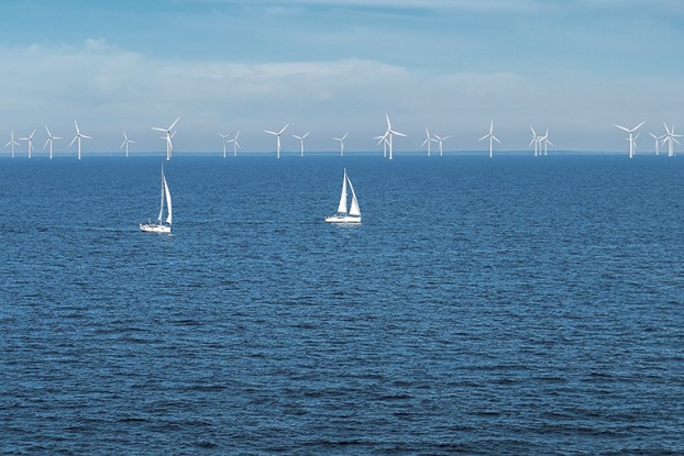 Alternative energy - row of offshore wind turbines and yachts at sea, green energy windmill generators at sea